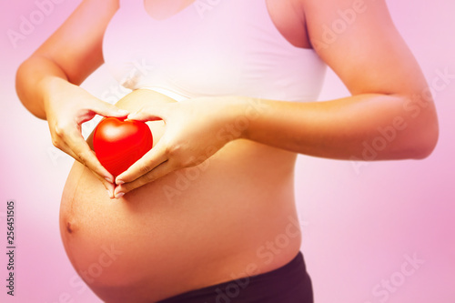In selective focus of small red heart was holding by pregnant woman hands,sign and symbol of love and care