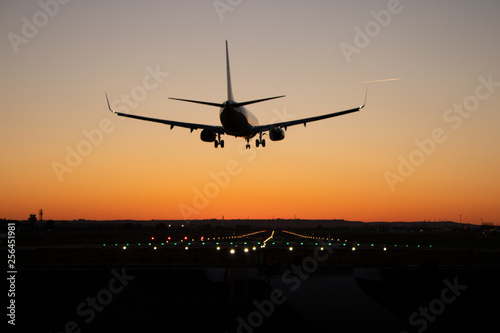 Commercial passenger airplane is landing on the airport runway during sunset