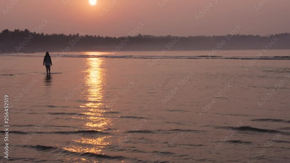 Female walking in water at Palolem beach, Goa, India. Sunset orange colours casting silhouette reflections across the waves. Female walking in water at Palolem beach, Goa, India. Sunset orange colours casting silhouette reflections across the waves.