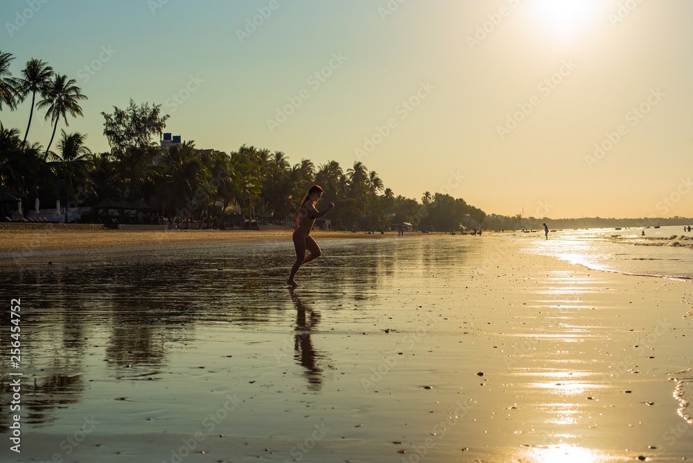 Woman runs barefoot on the beach at sunset. Silhouette of a woman by the sea at sunrise