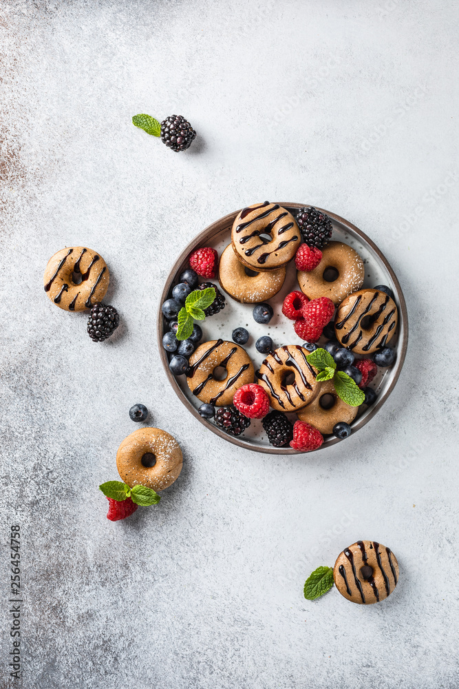 Homemade cinnamon and chocolate mini donuts on the plate with berries and mint on the light grey backgorund