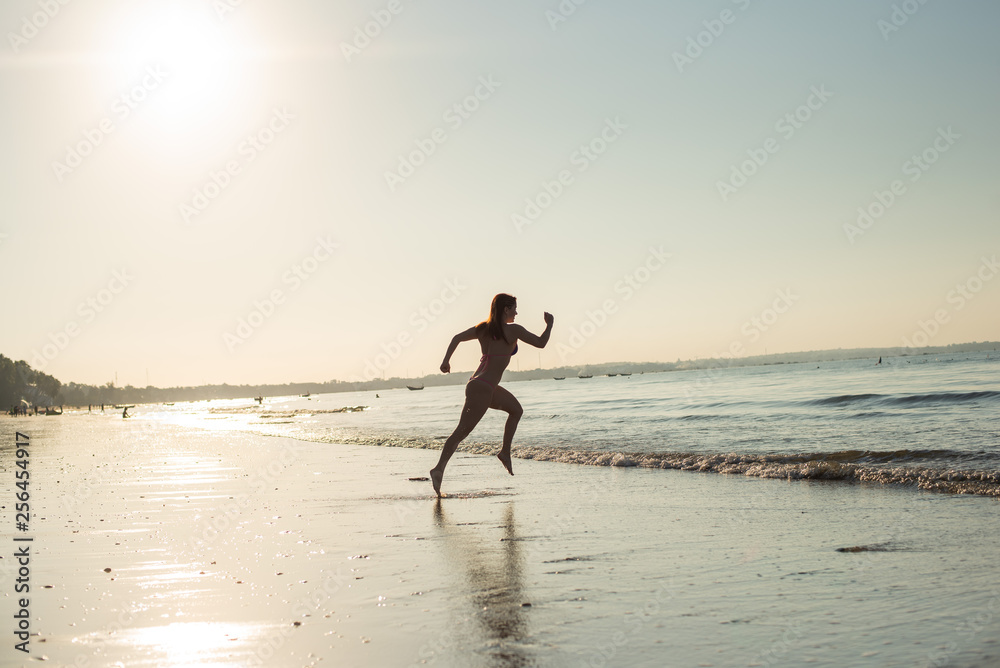 Woman runs barefoot on the beach at sunset. Silhouette of a woman by the sea at sunrise Woman runs barefoot on the beach at sunset. Silhouette of a woman by the sea at sunrise