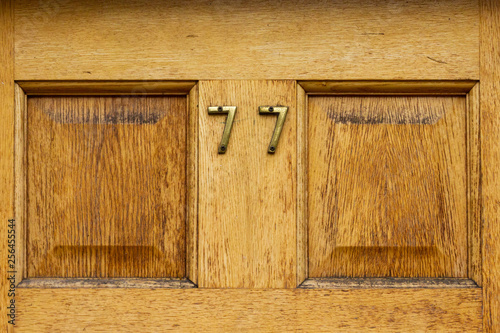 House number 77 with the seventy seven on a eyllow natural wood door photo