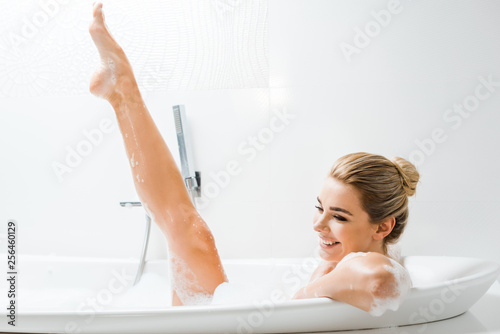 Fotografía attractive, smiling and blonde woman taking bath with foam in bathroom