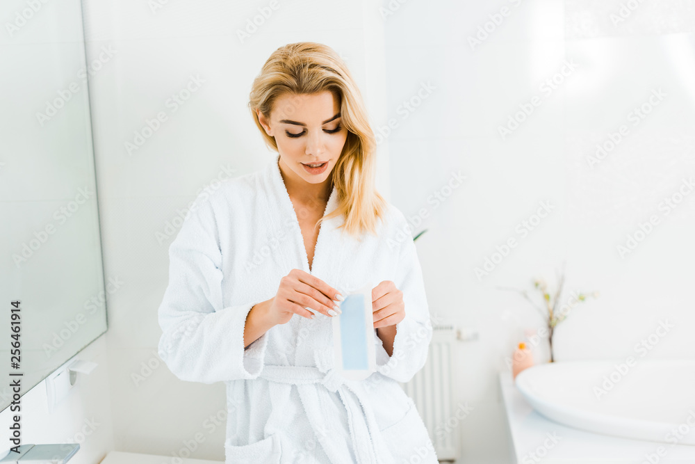 attractive woman in white bathrobe holding depilation stripe in bathroom attractive woman in white bathrobe holding depilation stripe in bathroom