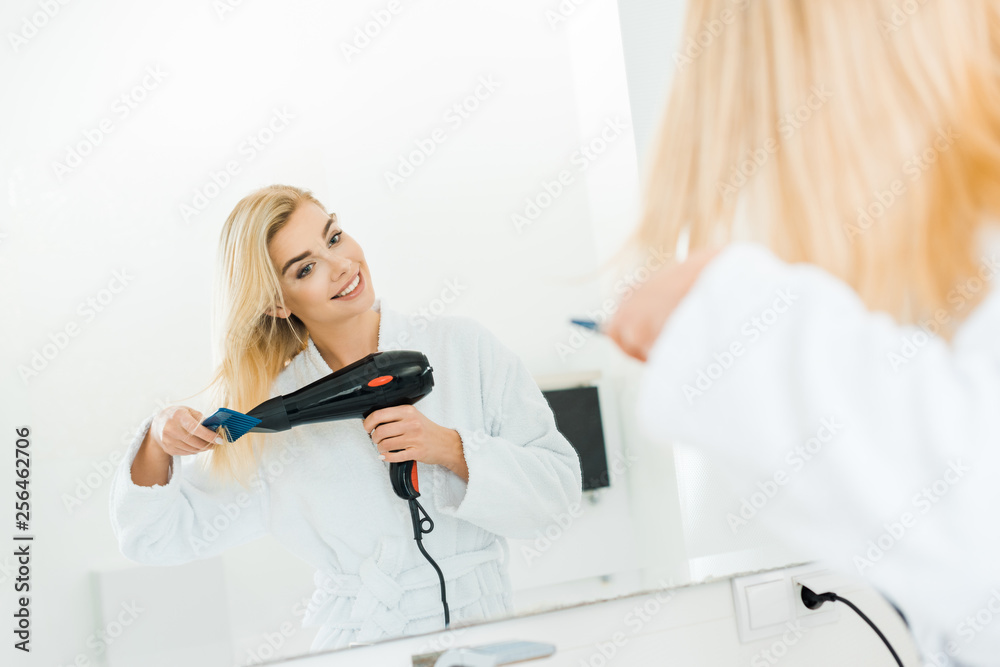 selective focus of beautiful and blonde woman in white bathrobe drying hair in bathroom selective focus of beautiful and blonde woman in white bathrobe drying hair in bathroom