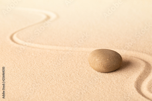 Concentration trough focus on a zen meditation stone. Round rock in sand texture background. Concept for yoga or spa welness treatment.