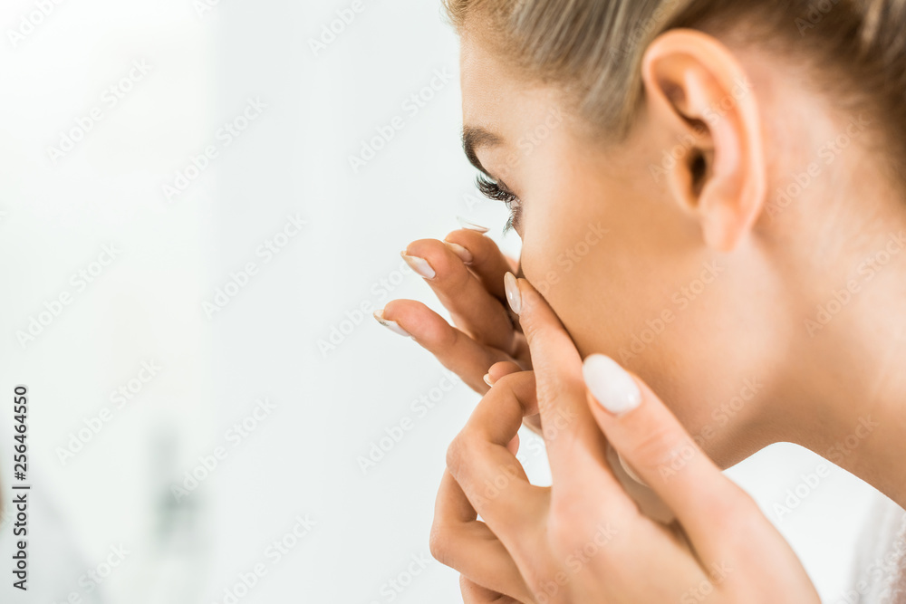 selective focus of attractive and blonde woman in white bathrobe attaching contact lens selective focus of attractive and blonde woman in white bathrobe attaching contact lens