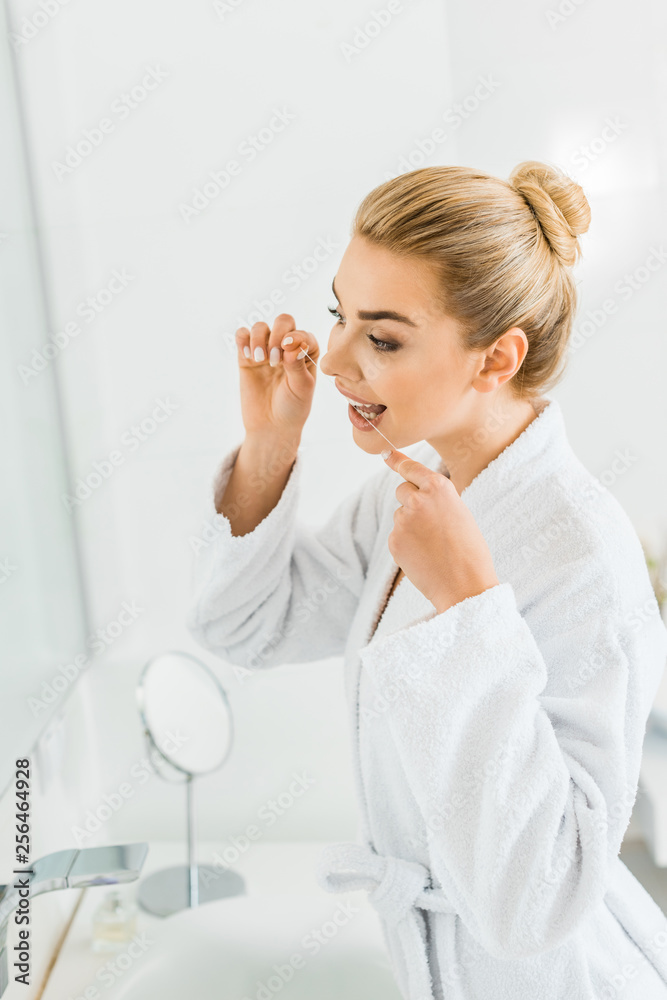 attractive and blonde woman in white bathrobe brushing teeth with dental floss attractive and blonde woman in white bathrobe brushing teeth with dental floss