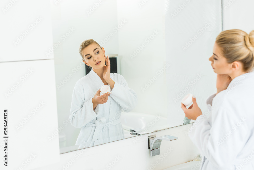 selective focus of beautiful woman in white bathrobe applying face cream in bathroom selective focus of beautiful woman in white bathrobe applying face cream in bathroom
