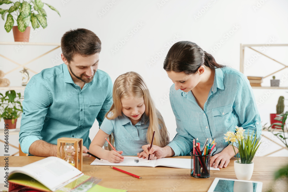 Father, mother and their daughter are smiling while spending time together. A day with family. Young happy couple with child are learning to draw. Education, studying and knowledge sharing concept. Father, mother and their daughter are smiling while spending time together. A day with family. Young happy couple with child are learning to draw. Education, studying and knowledge sharing concept.