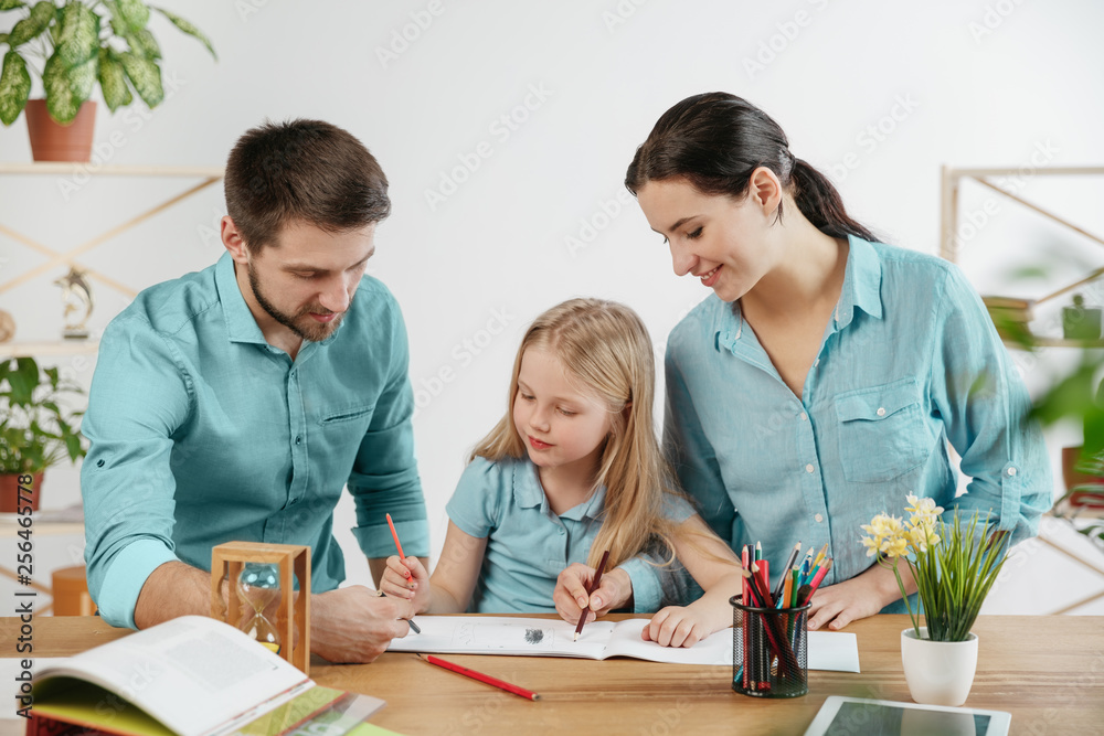 Father, mother and their daughter are smiling while spending time together. A day with family. Young happy couple with child are learning to draw. Education, studying and knowledge sharing concept. Father, mother and their daughter are smiling while spending time together. A day with family. Young happy couple with child are learning to draw. Education, studying and knowledge sharing concept.