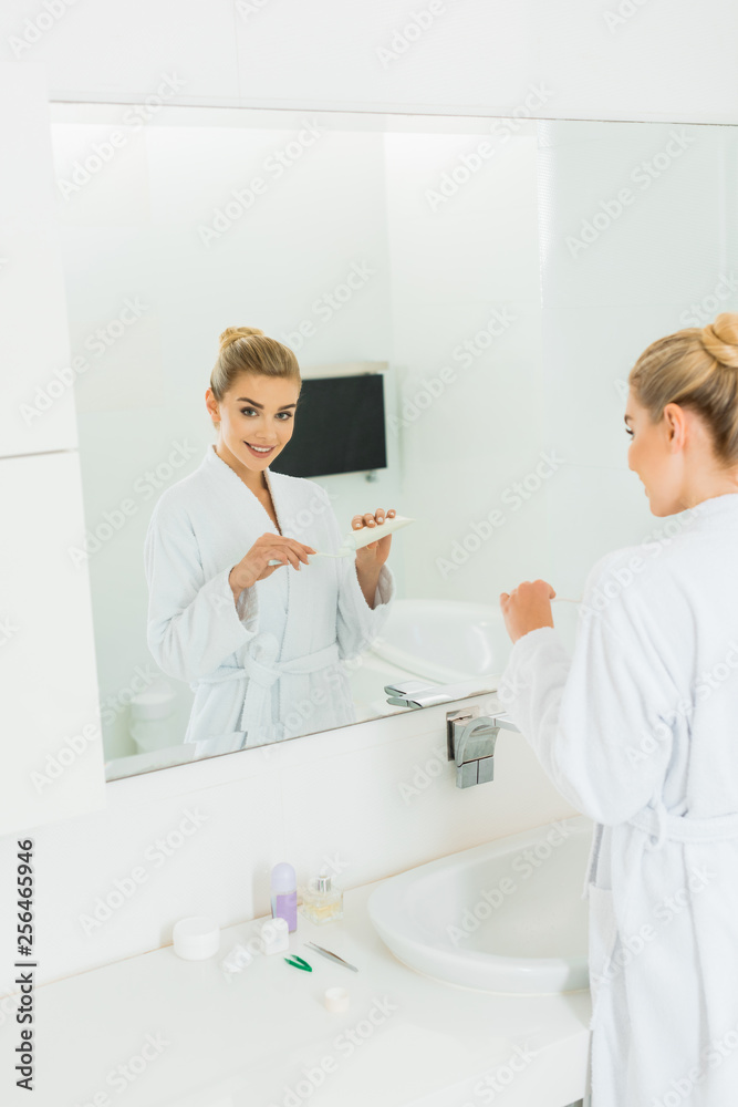 woman in bathrobe applying toothpaste on toothbrush and looking at mirror woman in bathrobe applying toothpaste on toothbrush and looking at mirror
