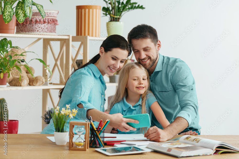 Father, mother and their daughter are smiling while spending time together. A day with family. Young happy couple with child are making a selfie with the smartphone. Education, studying and knowledge Father, mother and their daughter are smiling while spending time together. A day with family. Young happy couple with child are making a selfie with the smartphone. Education, studying and knowledge