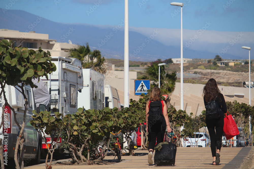 Young women walking along a road with heavy luggage El Medano, Tenerife, Canary, Islands, Spain)