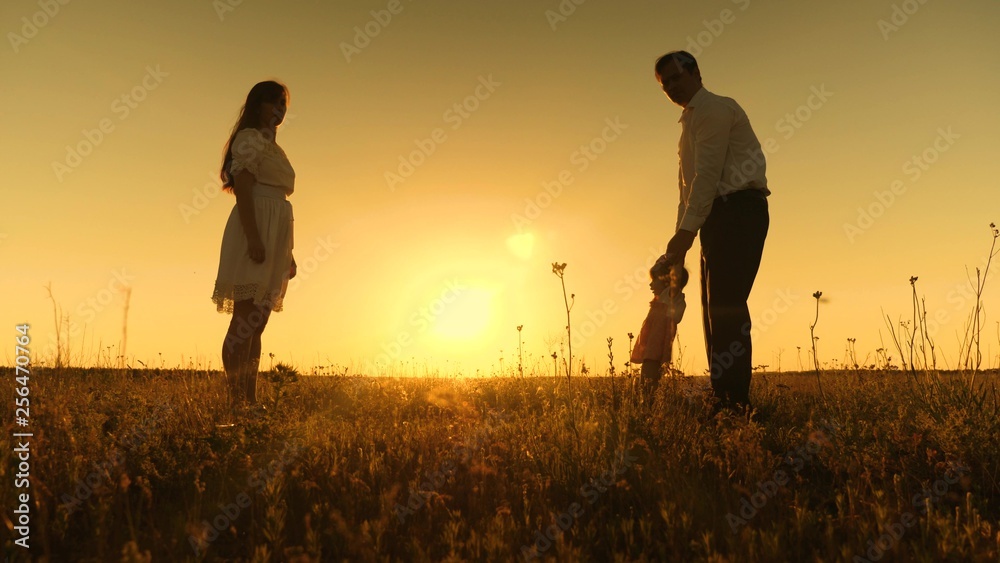 mom and dad are taught to go to small daughter, young beautiful family in park with child at sunset