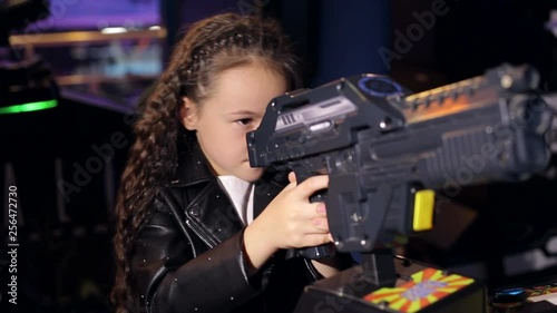 A little girl with long curly hair plays video games in a modern children's room. Modern shopping mall playground for kids and video games. photo