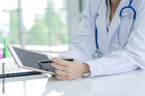 Doctor working with laptop computer and writing on paperwork. Hospital background.