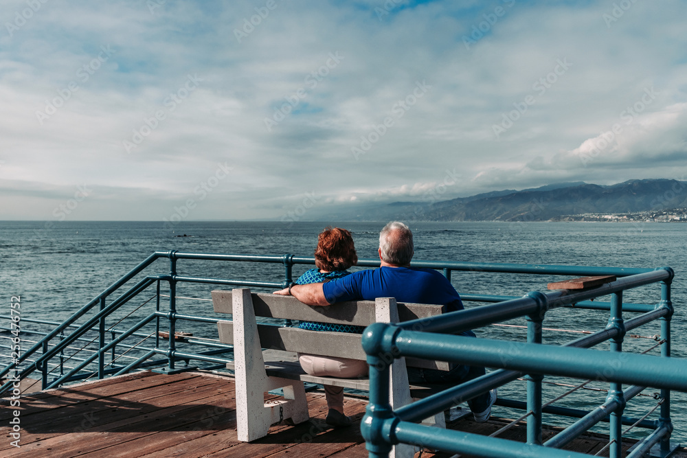 senior couple sitting on pier by the sea