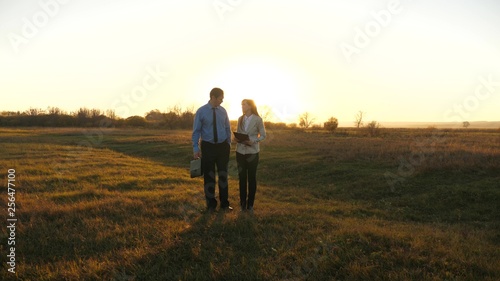 Business man with briefcase and business woman with tablet agree to work together at sunset and laugh. Business meeting with work partner.