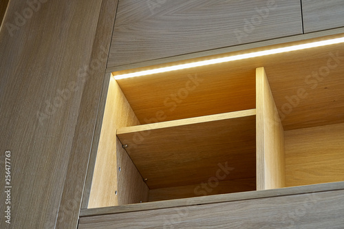 Wooden cupboard with drawers, empty shelves and LED lights. Modern furniture