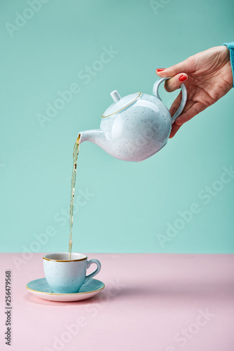 Tea pot pouring tea in a cup on blue backdrop