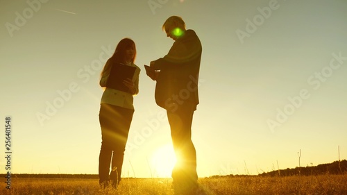 Business man with tablet and business woman with tablet discuss plan and schedule at sunset and laughs. Business meeting with working partner.