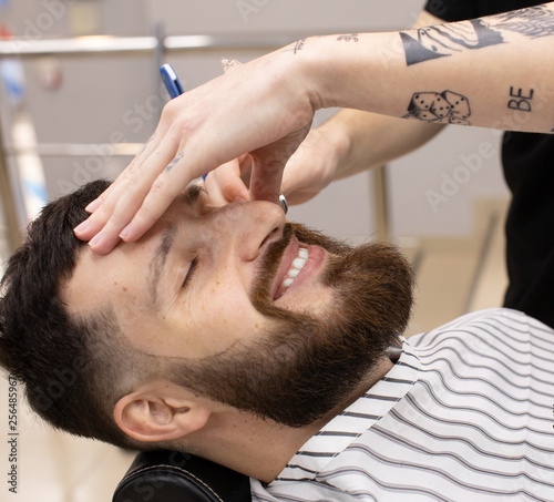 Shaving process of beards in Barbershop. Master makes a haircut beard client with vintage straight razor. 