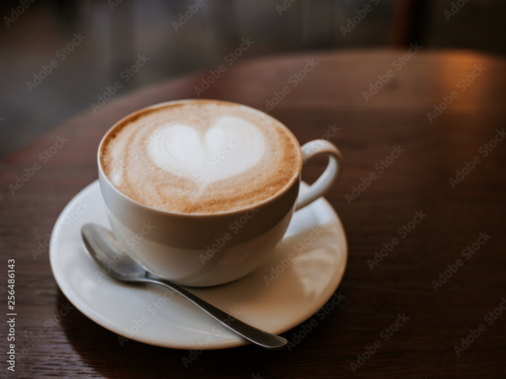 Fototapeta premium One cup of cappuccino with latte art on wooden table, white ceramic cup, place for text. Cafe culture.