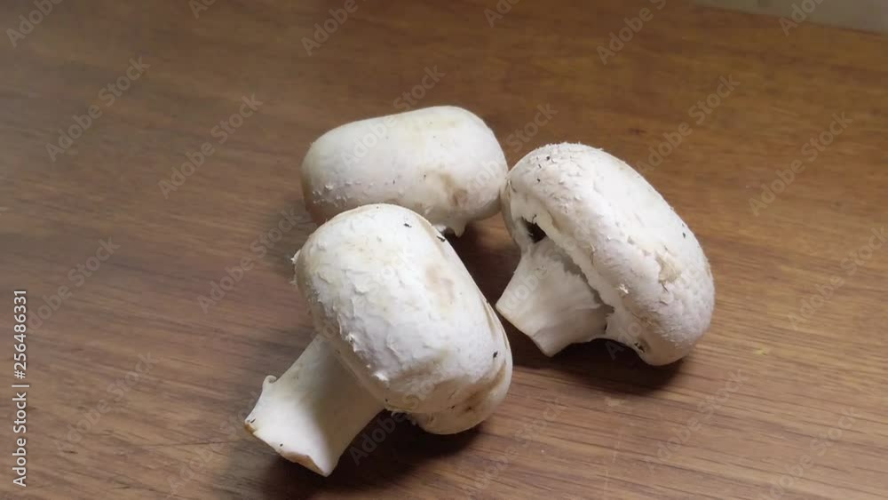 Slow motion hand picking individual white button close cup mushrooms from wooden surface. Slow motion hand picking individual white button close cup mushrooms from wooden surface.