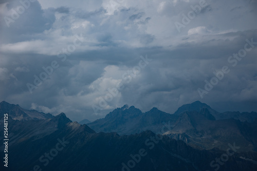 The peaks of the Caucasus Mountains in cloudy clouds and the rays of the sun through them in the outskirts of Dombai. And on the tops of snow lies.