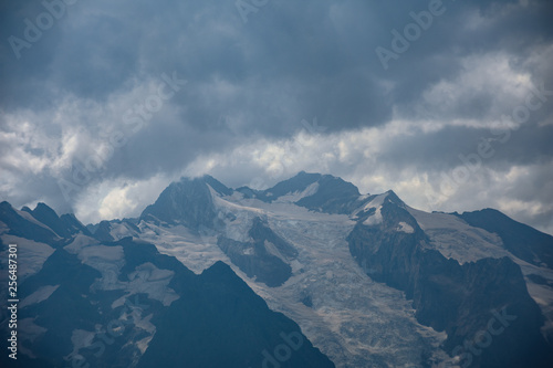 The peaks of the Caucasus Mountains in cloudy clouds and the rays of the sun through them in the outskirts of Dombai. And on the tops of snow lies. © dmitriydanilov62