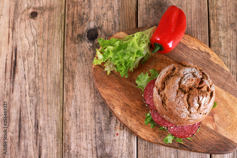 whole-grain bun topped with salad and salami sausage - freshly baked whole grain bun breakfast on rustic wooden table whole-grain bun topped with salad and salami sausage - freshly baked whole grain bun breakfast on rustic wooden table