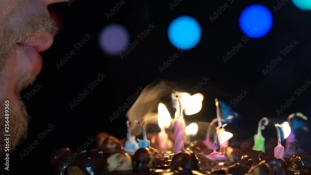 Birthday party, man blowing out colorful birthday candles on chocolate cake. Close-up 4K shot