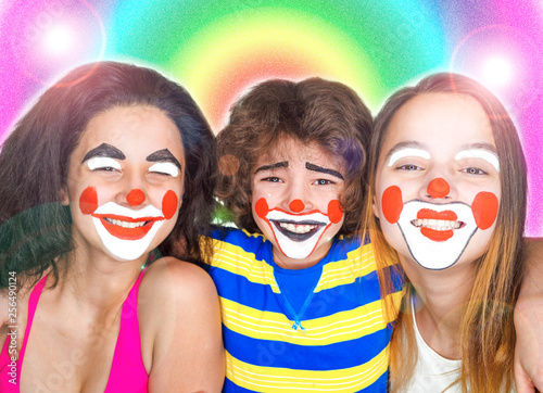 Two teen sisters and a little brother in the role of clowns posing bright colorful background. Family affection concept.
