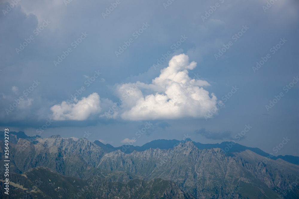 The peaks of the Caucasus Mountains in cloudy clouds and the rays of the sun through them in the outskirts of Dombai. And on the tops of snow lies.