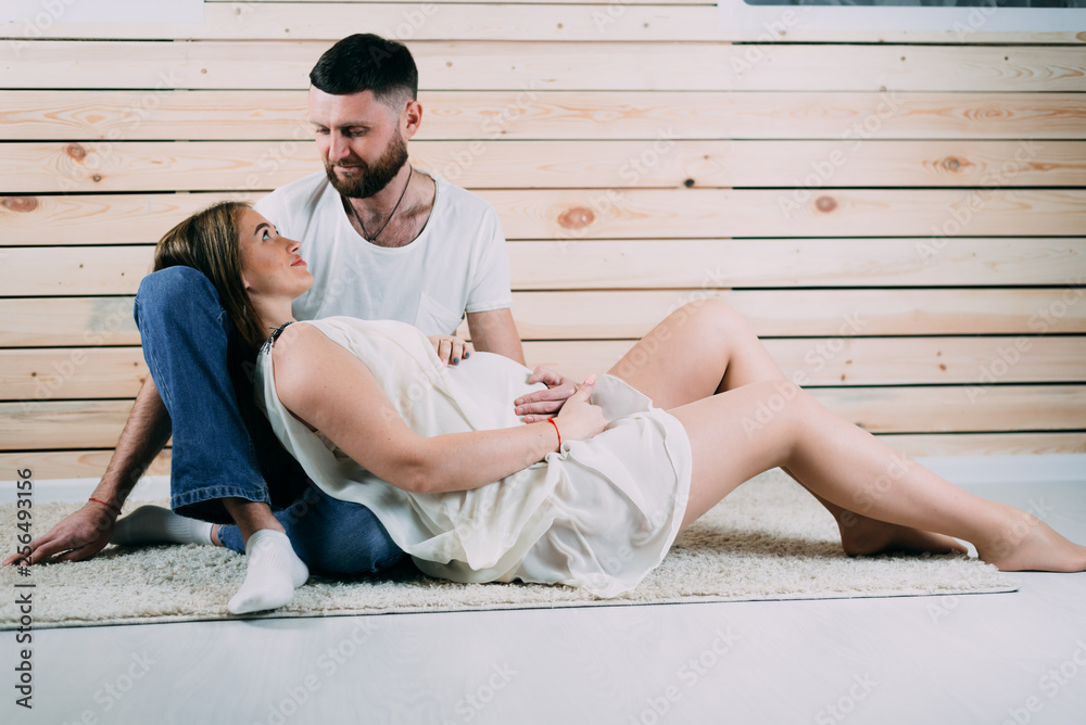 Young pregnant woman with husband sitting on floor on wooden background