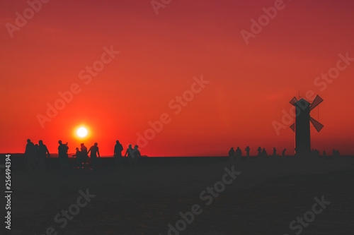A group of people after a hard day work returns to the mill, against the background of the sunset and the red surreal sky, the concept of hard physical work
