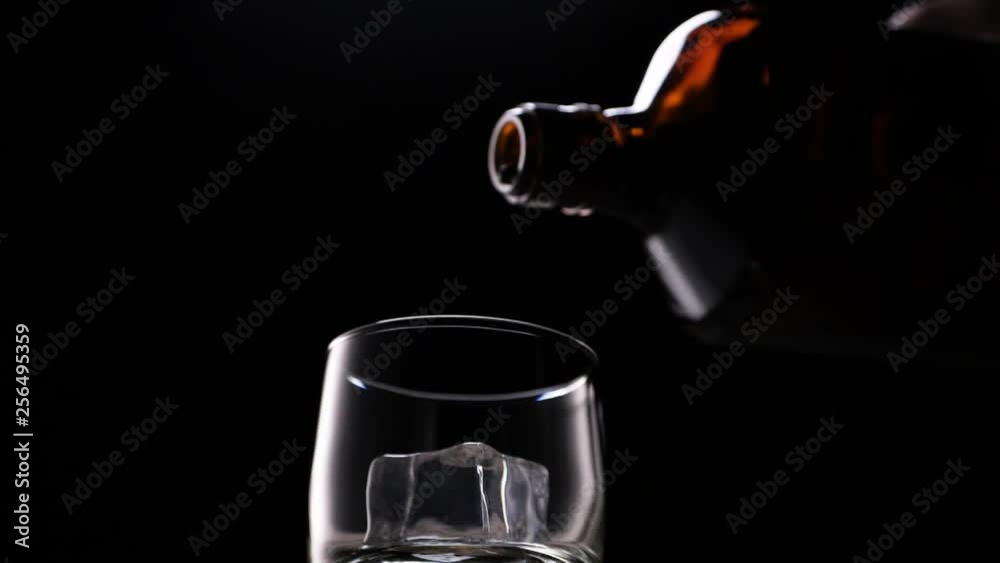 Golden whiskey pouring in the glass from the bottle. With ice cubes. Golden whiskey pouring in the glass from the bottle. With ice cubes.