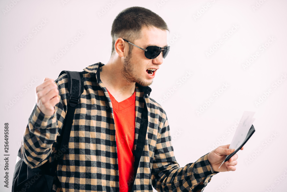 a man in sunglasses with a backpack tickets and a passport on a gray background a man in sunglasses with a backpack tickets and a passport on a gray background