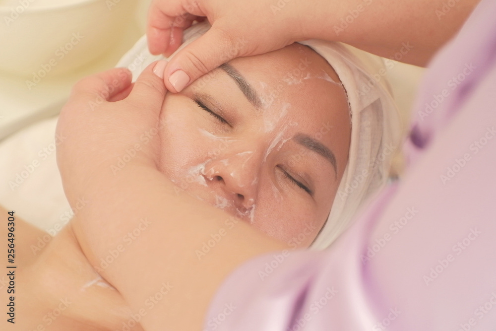 Close-up of the hand of a beautician makes a woman a facial massage with a cosmetic cream. Asian Woman takes kosmetologicheskie procedure. Healthy massage The concept of cosmetology.