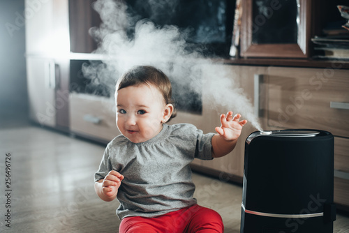 a little girl in red pants looks and touches the humidifier. Moisture in the house concept