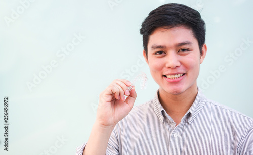 close up young asian man smiling with hand holding dental aligner retainer (invisible) at dental clinic for beautiful teeth treatment course concept	 photo