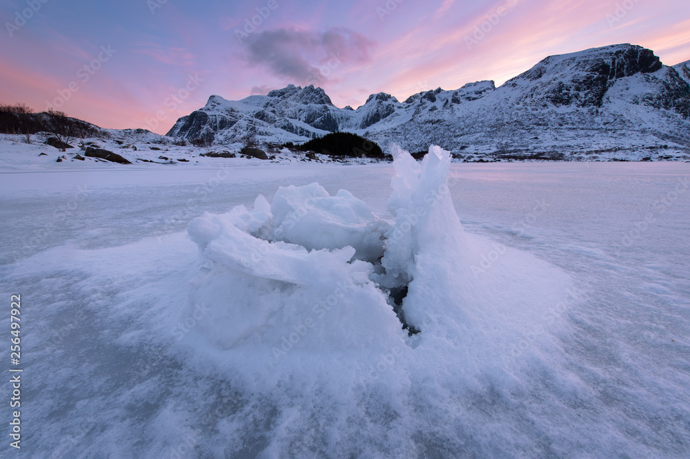 Beautiful landscape cracking ice, frozen sea coast with mountain ridge background at sunset in Lofoten Islands, winter season, Norway