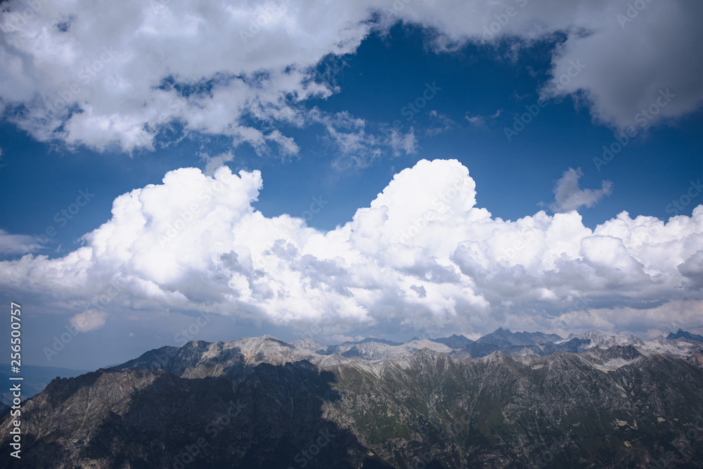 The peaks of the Caucasus Mountains in cloudy clouds and the rays of the sun through them in the outskirts of Dombai. And on the tops of snow lies. The peaks of the Caucasus Mountains in cloudy clouds and the rays of the sun through them in the outskirts of Dombai. And on the tops of snow lies.