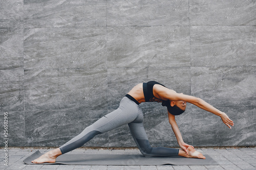 Pretty lady training in a summer city. Brunette doing yoga. Gitl in a sportsuit