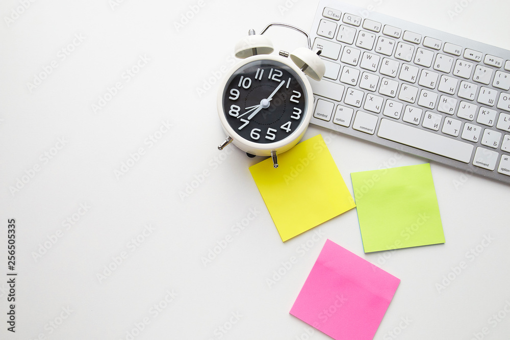 Office desk table with keyboard and alarm clock on white background, stickers yellow, purple and green color. Top view and copy space, flat lay Office desk table with keyboard and alarm clock on white background, stickers yellow, purple and green color. Top view and copy space, flat lay