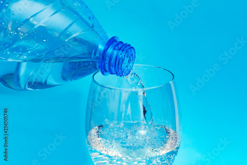 clean, clear cool mineral water is poured from a plastic bottle into a clear glass glass goblet
