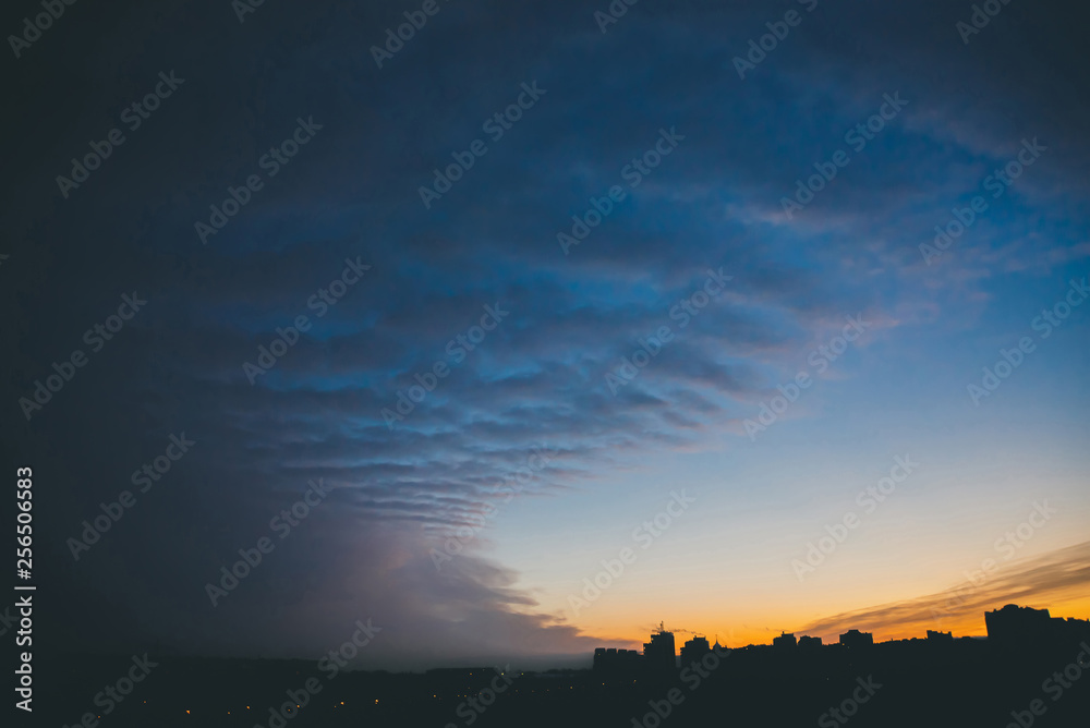 Obraz premium Cityscape with wonderful varicolored vivid dawn. Amazing dramatic blue cloud sky above dark silhouettes of city building roofs. Atmospheric background of orange sunrise in overcast weather. Copy space