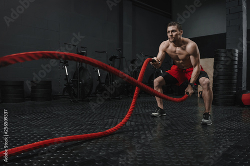 Young crossfit athlete doing battle ropes exercise at the fitness gym.